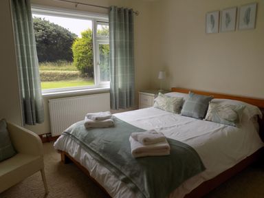 A bedroom with a bed with pillows and folded towels a chair by the window and three framed pictures on the wall at Brookfield in St Gennys near Wainhouse Corner
