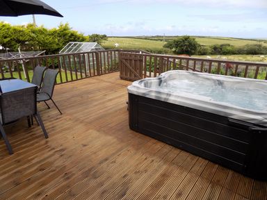 An outdoor wooden deck with a hot tub table with four chairs a patio umbrella and a glass greenhouse in the background at Brookfield in St Gennys near Wainhouse Corner