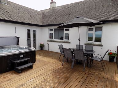 An outdoor patio with wooden decking a hot tub a table with six chairs and a large umbrella at Brookfield in St Gennys near Wainhouse Corner