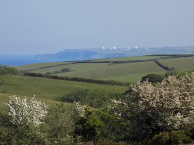 A countryside landscape with green fields trees and satellite dishes on a distant hill at Brookfield in St Gennys near Wainhouse Corner