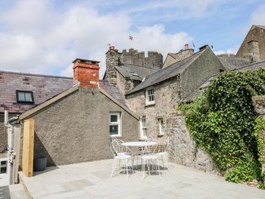 An outdoor patio with a white metal table and four chairs surrounded by stone buildings and greenery at 10 Westgate Hill in Pembroke