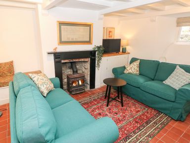 A living room with two green sofas a red patterned rug a wood burning stove and a small black round table at 10 Westgate Hill in Pembroke