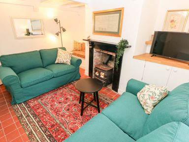 A living room with two green sofas a red patterned rug a black wood stove a small black round table a television and framed pictures at 10 Westgate Hill in Pembroke