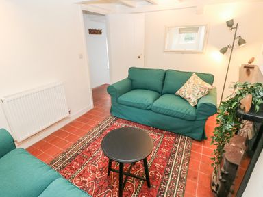 A living room with two green sofas a round black table a red patterned rug and a floor lamp at 10 Westgate Hill in Pembroke
