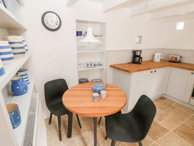 A kitchen with a round wooden table and two black chairs near white cabinets and shelves with crockery at 10 Westgate Hill in Pembroke