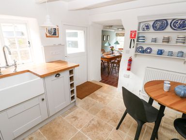 A kitchen with a wooden countertop a white sink a small round wooden table with black chairs and a shelf with blue and white dishes at 10 Westgate Hill in Pembroke