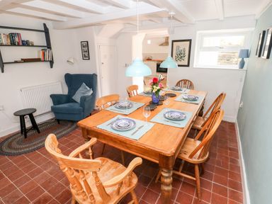 A dining room with a wooden table set for six people with blue and white plates and light blue placemats with a blue armchair and a small black table on a rug at 10 Westgate Hill in Pembroke