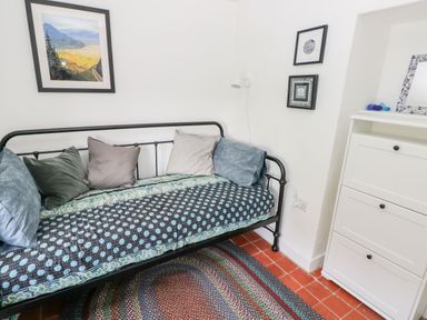 A small room with a black metal daybed with cushions a white cabinet with three drawers and framed pictures on the white walls at 10 Westgate Hill in Pembroke