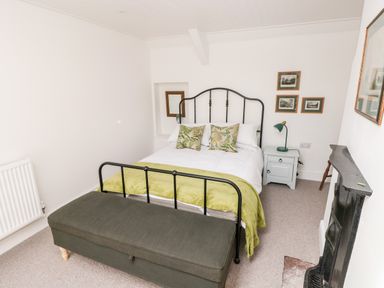 A bedroom with a bed, green bench, nightstand with lamp, framed pictures, and a fireplace at 10 Westgate Hill in Pembroke
