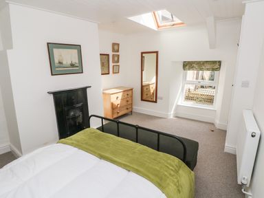 A bedroom with a black metal bed frame a wooden chest of drawers a wall mirror and a window with a skylight at 10 Westgate Hill in Pembroke