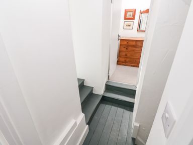 A narrow hallway with painted wooden steps leading to a room with a wooden dresser and framed pictures on the wall at 10 Westgate Hill Pembroke