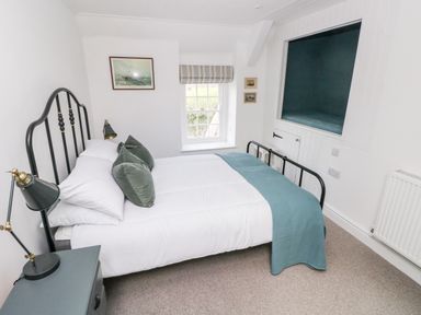 A bedroom with a double bed with green pillows and blue blanket a bedside table with a lamp a window and built in storage at 10 Westgate Hill in Pembroke