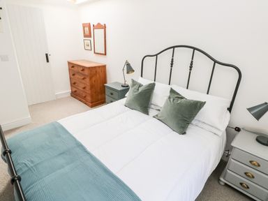 A bedroom with a bed a black metal headboard bedside tables with lamps a wooden chest of drawers and wall mirror at 10 Westgate Hill in Pembroke