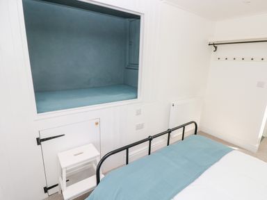 A bedroom with a bed covered by a blue blanket a small white step stool a built in bed alcove and wall hooks at 10 Westgate Hill in Pembroke