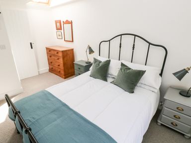 A bedroom with a double bed with white bedding and green pillows two bedside tables with lamps a wooden chest of drawers and a mirror on the wall at 10 Westgate Hill in Pembroke