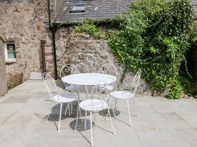 A white metal patio table with four matching chairs on a stone patio next to a stone wall with ivy at 10 Westgate Hill in Pembroke