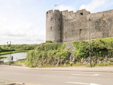 An exterior view of a stone castle with a round tower and a flag on top next to a road and a river at 10 Westgate Hill in Pembroke