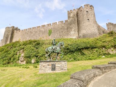 A statue of a horse and rider on a stone pedestal in front of a large stone castle with battlements and flags on top at 10 Westgate Hill in Pembroke