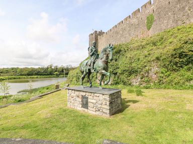 A bronze statue of a knight on a horse on a stone pedestal beside a castle wall near a river at 10 Westgate Hill in Pembroke