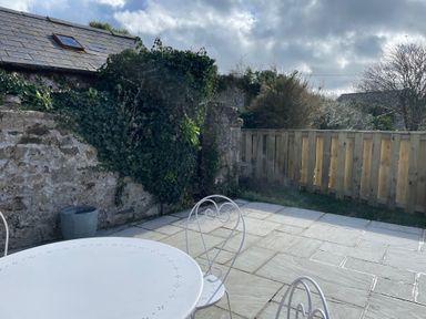 An outdoor patio with a white metal table and chairs next to a stone wall covered in ivy and a wooden fence at 10 Westgate Hill in Pembroke