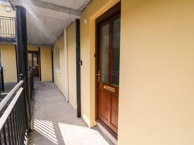 An outdoor corridor with yellow walls and brown wooden doors at 2 Garnish Court in Glengarriff County Cork