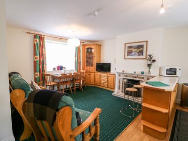 A living room with wooden chairs a dining table television fireplace and a microwave at 2 Garnish Court in Glengarriff County Cork