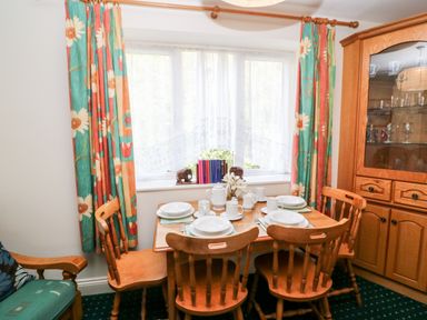 A dining room with wooden table and chairs set with white dishes and floral curtains at 2 Garnish Court in Glengarriff County Cork