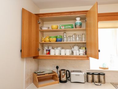 An open kitchen cabinet with mugs glasses and bowls above a counter with a kettle toaster and three canisters at 2 Garnish Court in Glengarriff County Cork