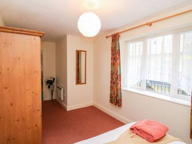 A bedroom with a bed, folded towels, a wooden wardrobe, a mirror on wall, a window with curtains, and a vase with flowers at 2 Garnish Court in Glengarriff County Cork