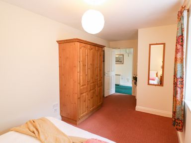 A bedroom with a wooden wardrobe a bed with yellow blanket a wall mirror and a window with colorful curtains at 2 Garnish Court in Glengarriff County Cork