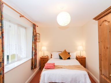 A bedroom with a double bed two bedside tables with lamps a window with curtains and a wooden wardrobe at 2 Garnish Court in Glengarriff County Cork