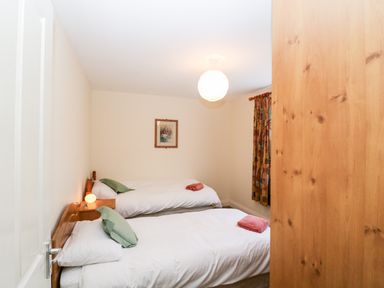 A bedroom with two single beds green pillows and towels on beds a wooden wardrobe and a framed picture on the wall at 2 Garnish Court in Glengarriff County Cork