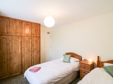 A bedroom with two single beds wooden wardrobes and a bedside table with a lamp at 2 Garnish Court in Glengarriff County Cork