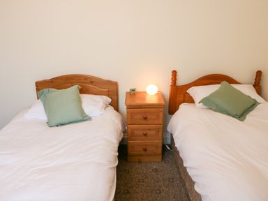 A bedroom with two single beds with green cushions and a wooden nightstand with a lamp at 2 Garnish Court in Glengarriff County Cork