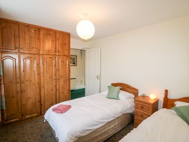 A bedroom with two single beds a wooden wardrobe and a wooden nightstand at 2 Garnish Court in Glengarriff County Cork