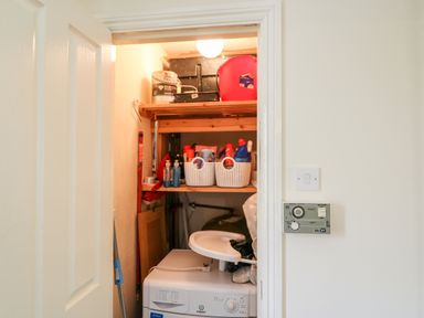 A small utility room with a washing machine shelves with cleaning supplies and a light switch at 2 Garnish Court in Glengarriff County Cork