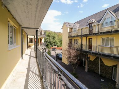 A balcony with black metal railing overlooking a courtyard with parked cars and yellow buildings at 2 Garnish Court in Glengarriff County Cork