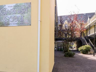 A courtyard with yellow buildings a sign for Garnish Court a tree and shrubbery in Glengarriff County Cork