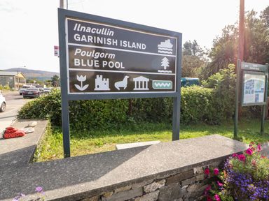 A road sign pointing to Garnish Island and Blue Pool near a stone wall with flowers in Glengarriff County Cork