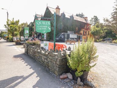 A stone wall with green plants and signs for Quills customer car park near a building with ivy at 2 Garnish Court in Glengarriff County Cork