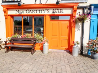 The orange entrance of Mac Carthys Bar with a wooden bench and flower pots outside