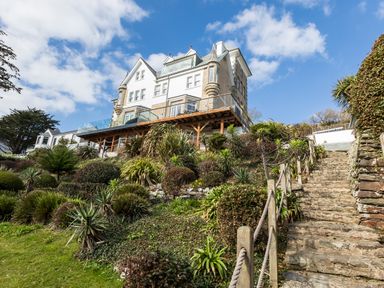 A stone stairway with rope railing leading up to a large house on a hill with plants and shrubs at The Tower 5 Corisande Manor in Newquay