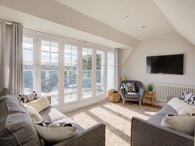 A living room with two sofas armchair wall mounted TV and glass doors leading to a balcony at The Tower 5 Corisande Manor in Newquay