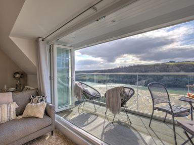 A balcony with chairs and a table overlooking a river and hills at The Tower 5 Corisande Manor in Newquay
