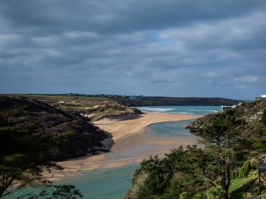 A beach with a river flowing into the sea surrounded by hills and greenery at The Tower 5 Corisande Manor in Newquay