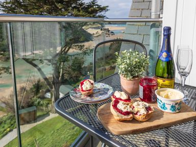 A balcony table with scones with jam and cream a bottle of champagne two glasses and a potted plant at The Tower 5 Corisande Manor in Newquay