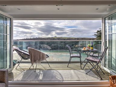 A balcony with chairs a small table and glass railing overlooking a river and hills at The Tower 5 Corisande Manor in Newquay