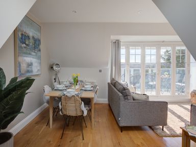 A dining area with a wooden table set for six and a gray sofa next to glass doors leading to a balcony at The Tower 5 Corisande Manor in Newquay