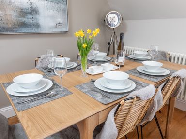 A dining table set with white dishes wine glasses and a vase of yellow flowers at The Tower 5 Corisande Manor in Newquay