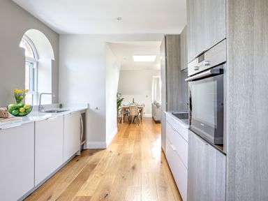 A kitchen with wooden floor, white cabinets, a built-in oven, and a dining table in the background at The Tower 5 Corisande Manor in Newquay